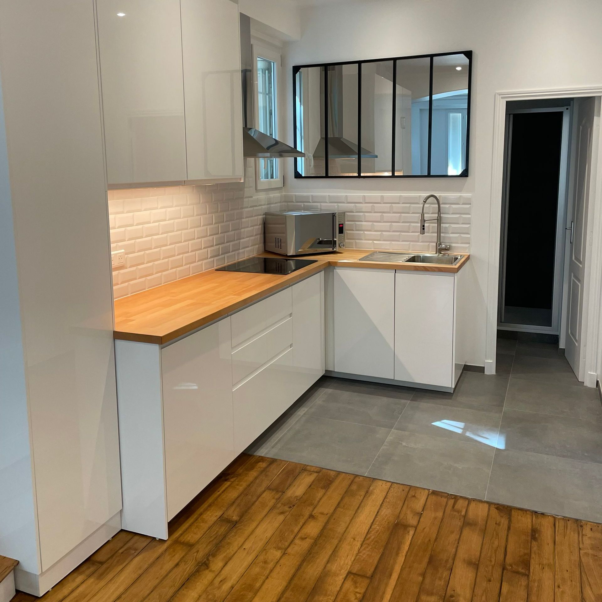 Une cuisine rénovée avec des meubles blancs et un grand miroir.