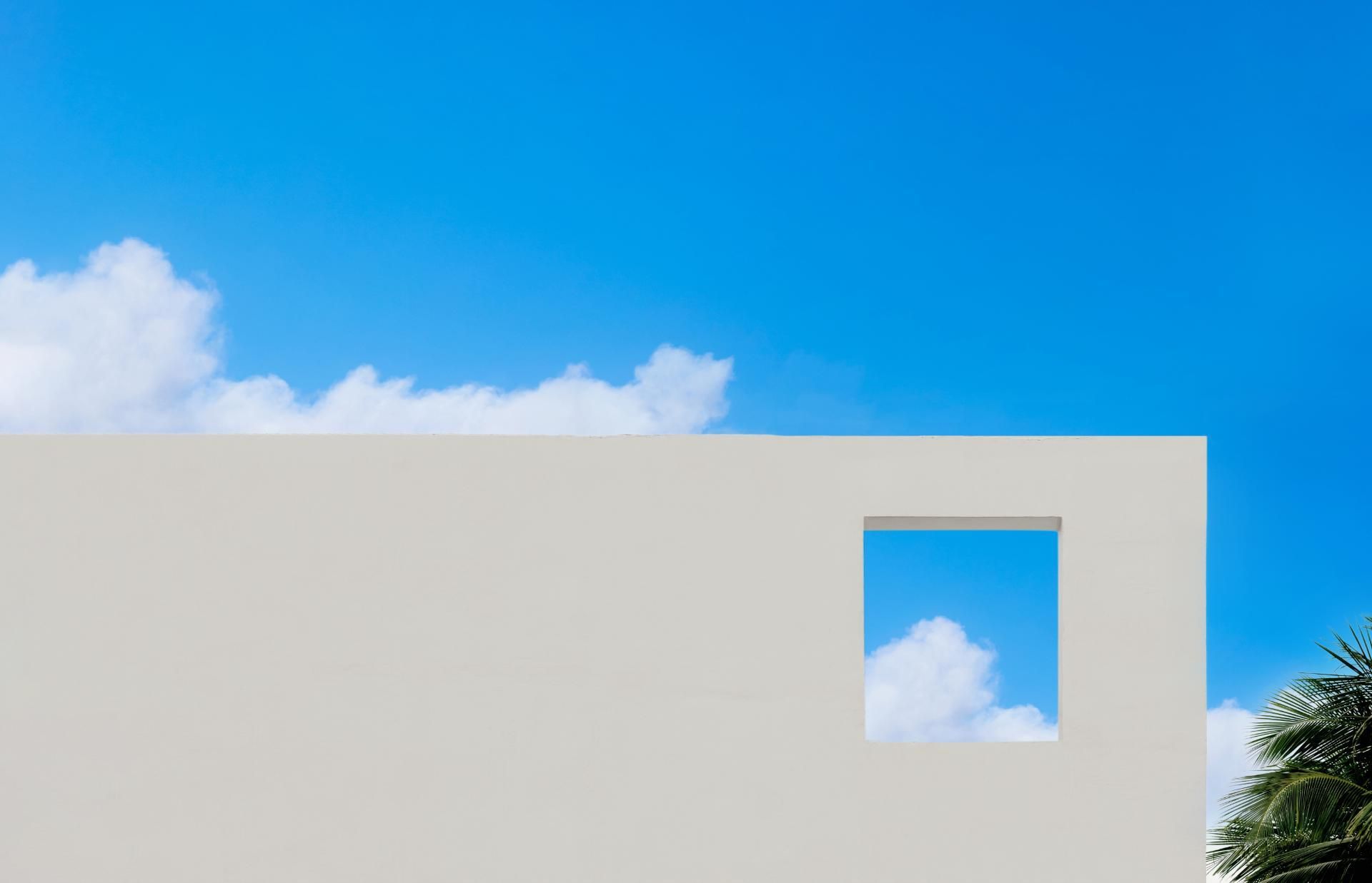 eine weiße Wand mit einem quadratischen Fenster und einem blauen Himmel dahinter