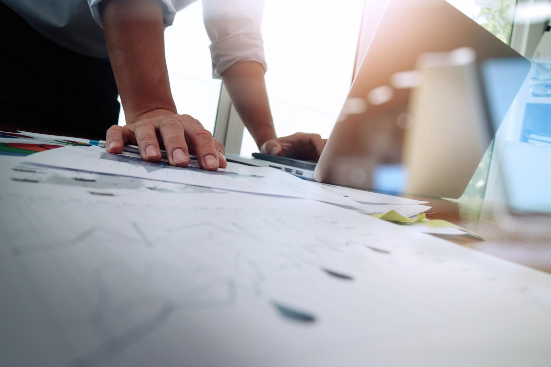 eine Person schaut auf ein Blatt Papier , während sie an einem Laptop arbeitet