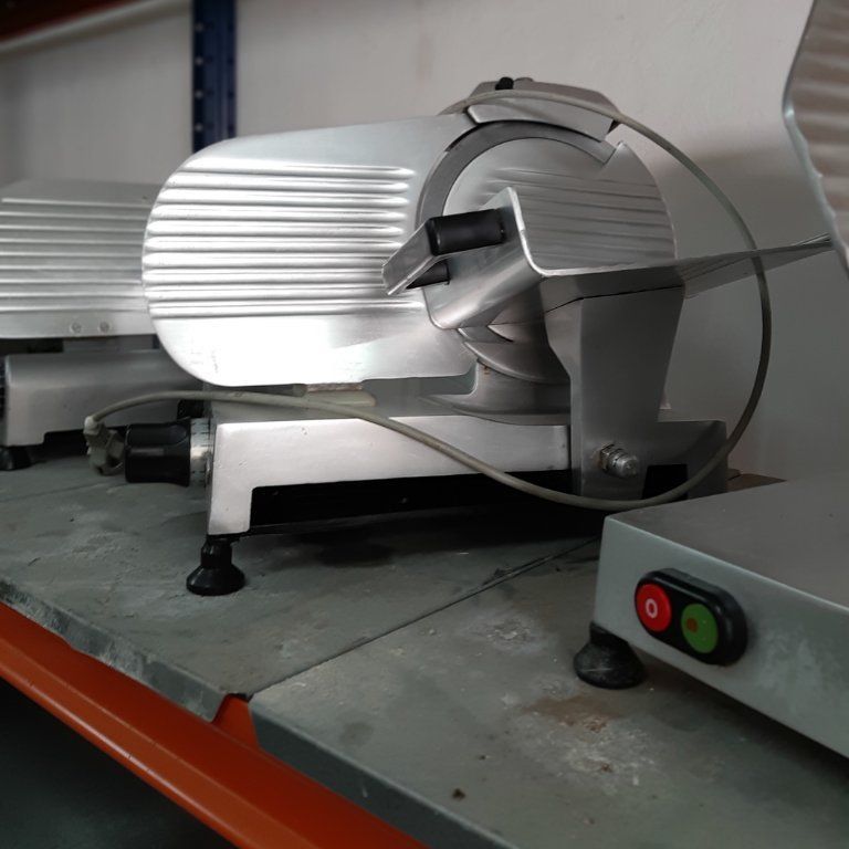 Una cortadora de carne está en un estante junto a otra máquina.