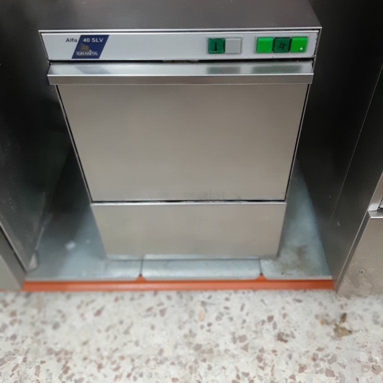 Un lavavajillas de acero inoxidable está sobre un suelo de baldosas.