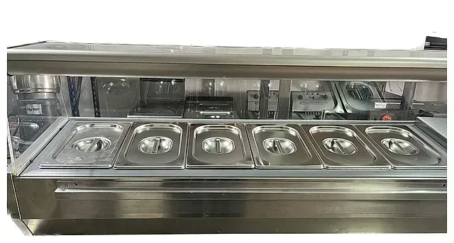 Una vitrina de alimentos de acero inoxidable con tapa de vidrio en una cocina.