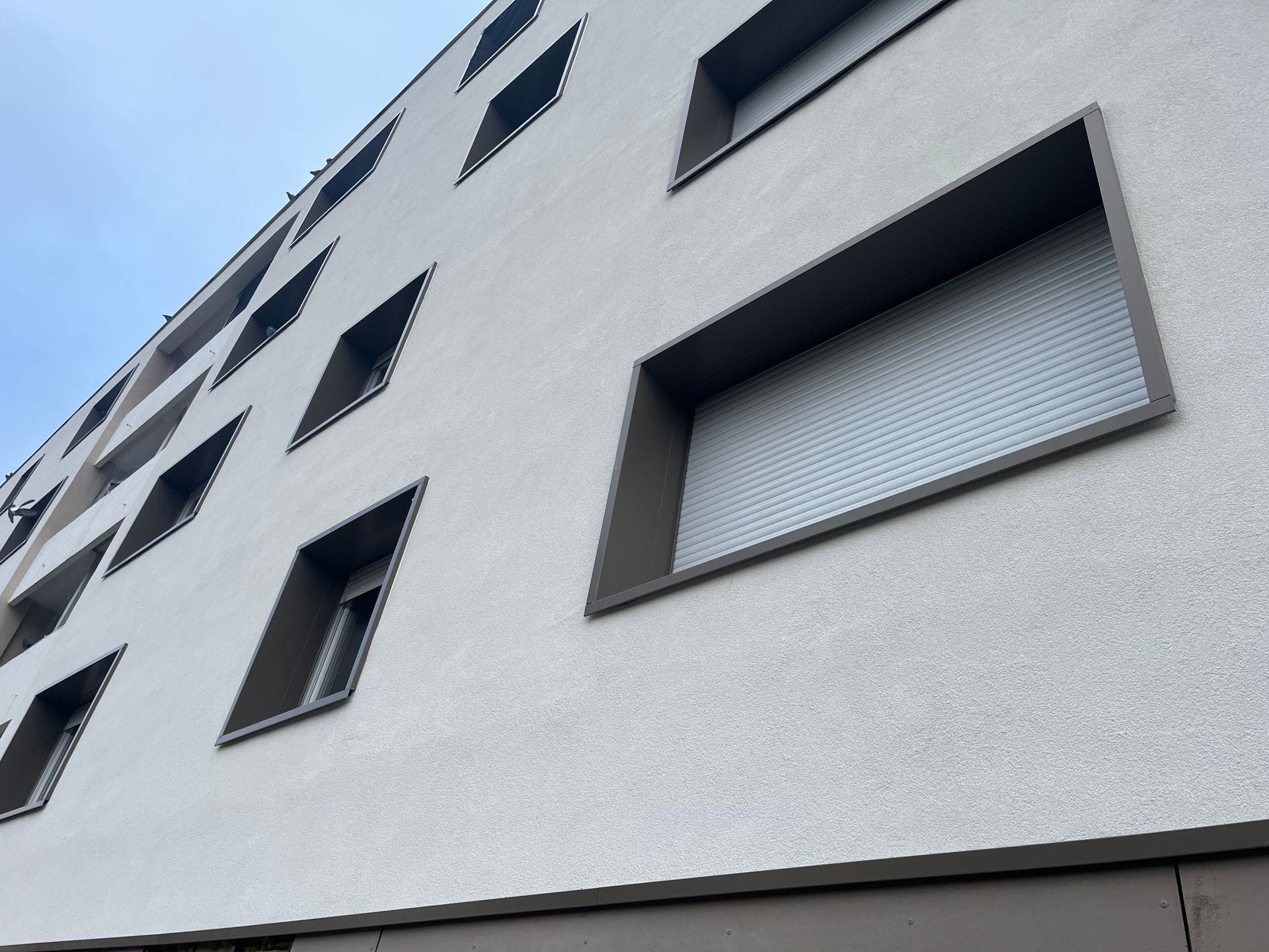 Bâtiment moderne aux fenêtres rectangulaires, façade grise et blanche, perspective oblique.