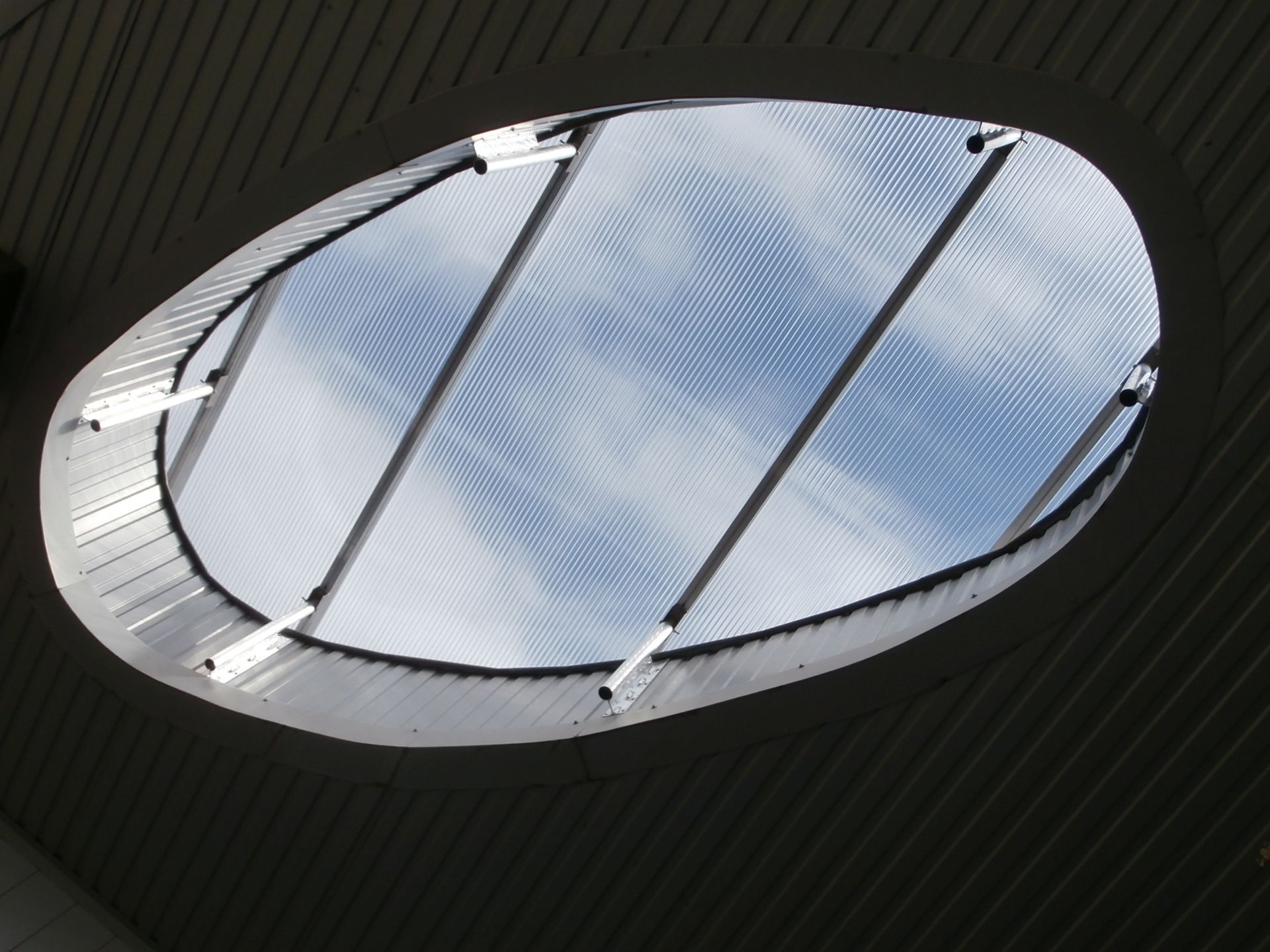 Puits de lumière ovale, laissant apparaître le ciel bleu à travers une structure en plastique texturé.
