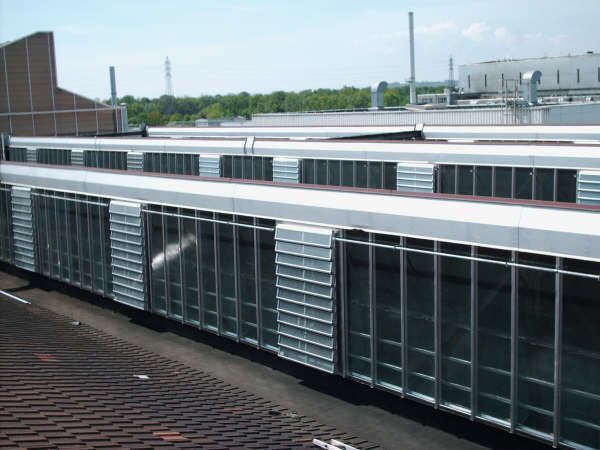 Toit-terrasse avec de longues baies vitrées de style industriel et des grilles de ventilation métalliques.