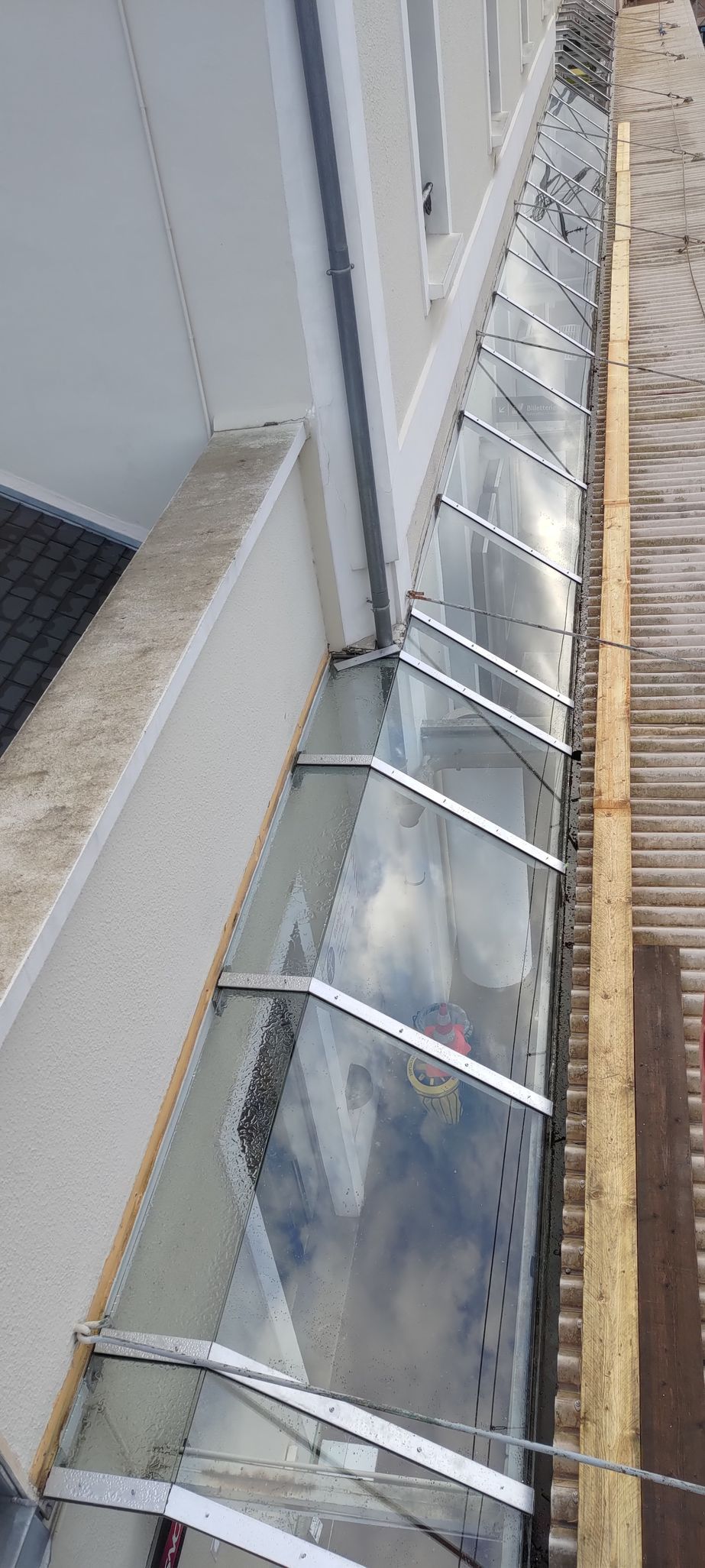 Une gouttière de toit transparente et limpide, fixée par des supports métalliques attachés au côté du bâtiment et au toit.