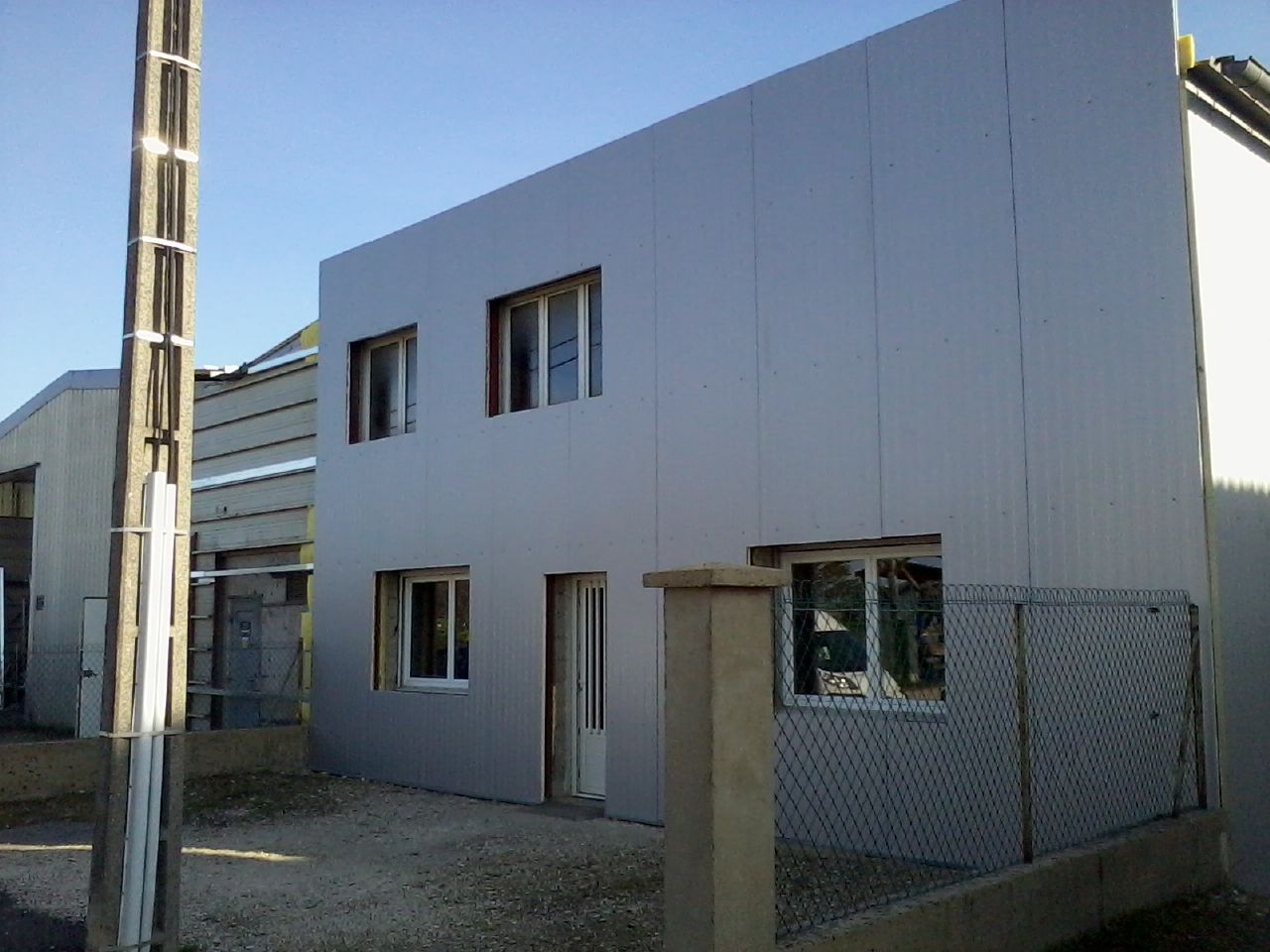 Bâtiment gris de deux étages avec des fenêtres à cadre blanc, une porte et un lampadaire.