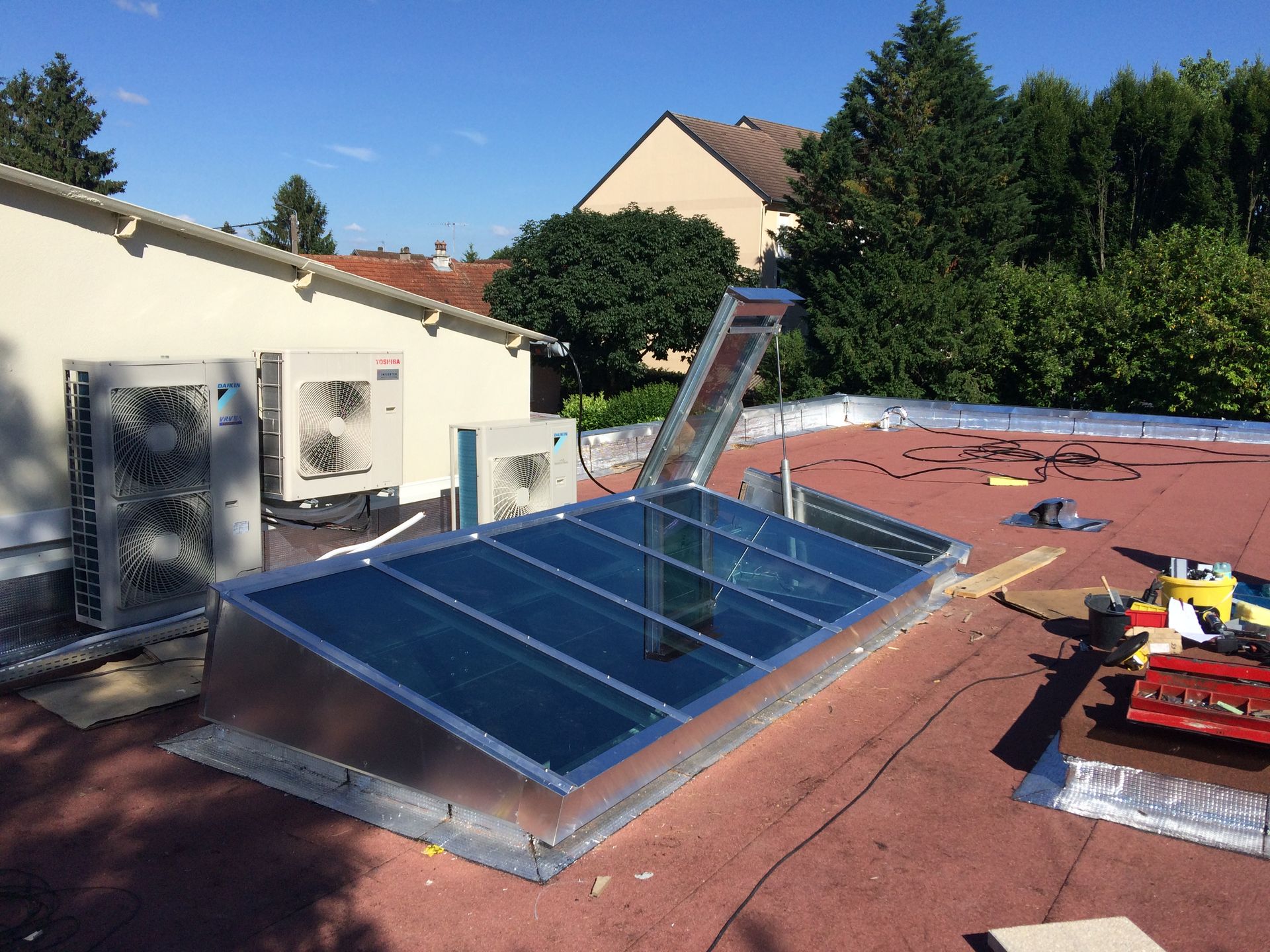 Puits de lumière installé sur un toit rouge avec unités de climatisation.