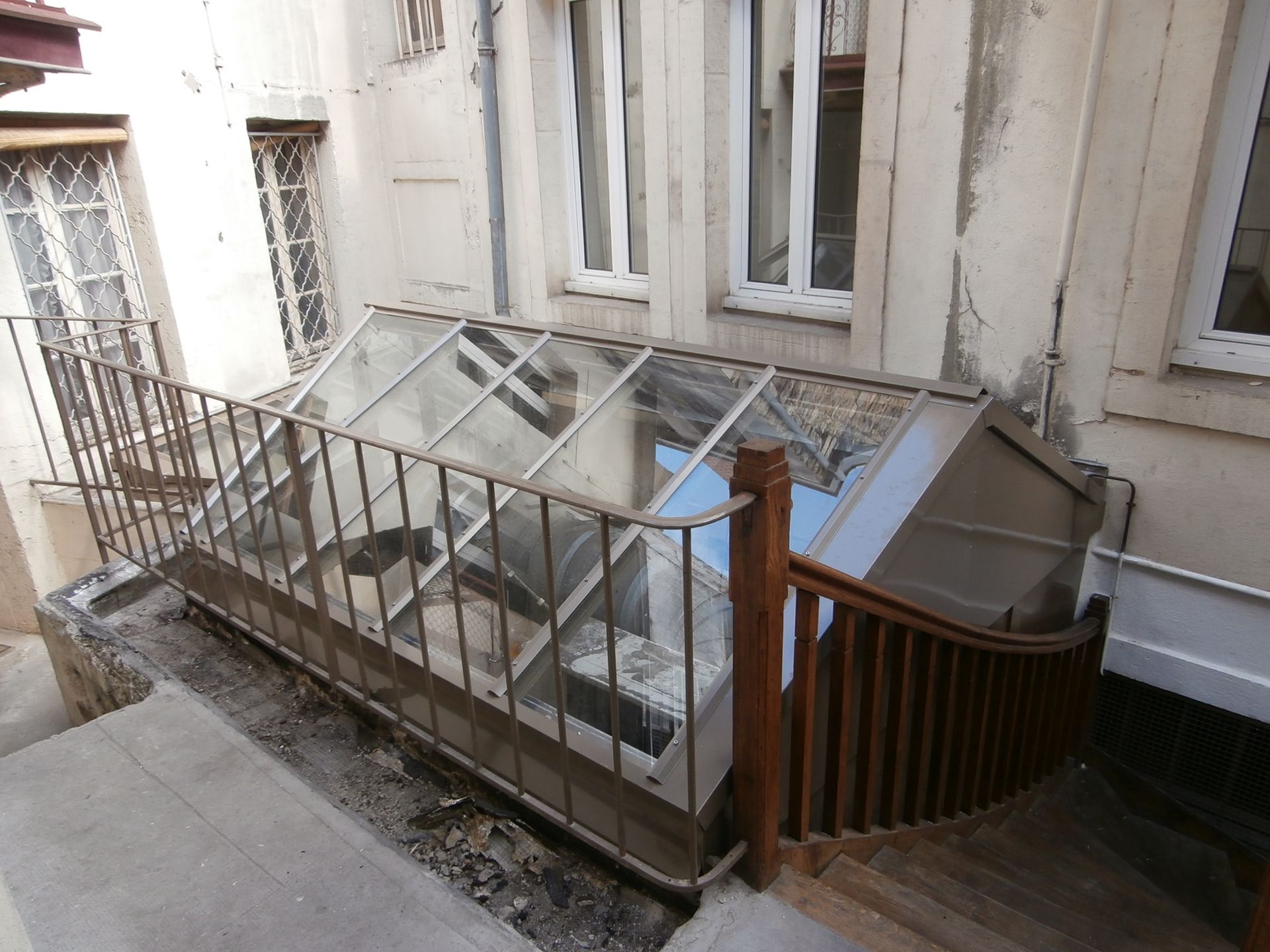 Escalier extérieur descendant vers une entrée vitrée.