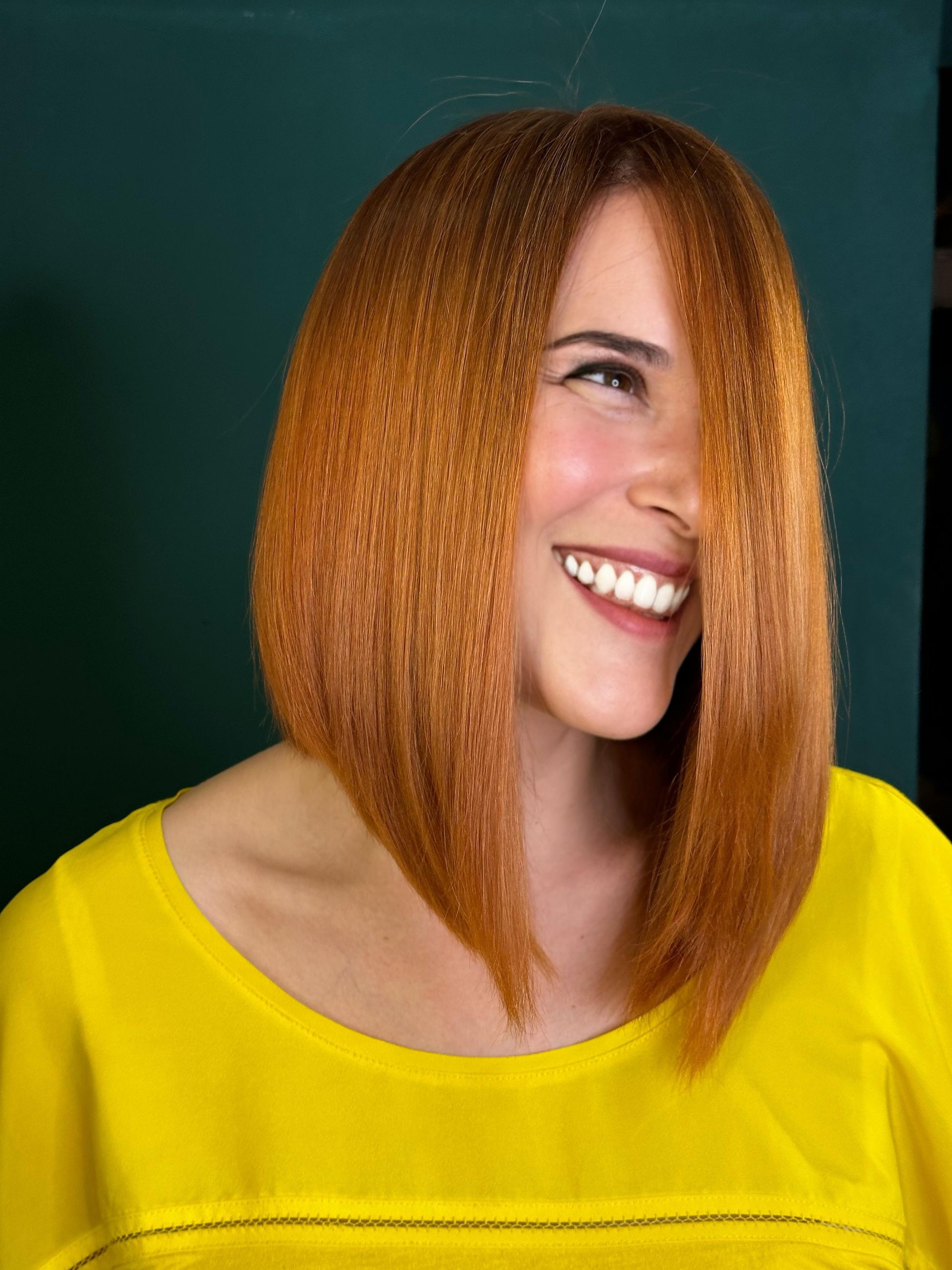 Una mujer pelirroja lleva una camisa amarilla y sonríe.