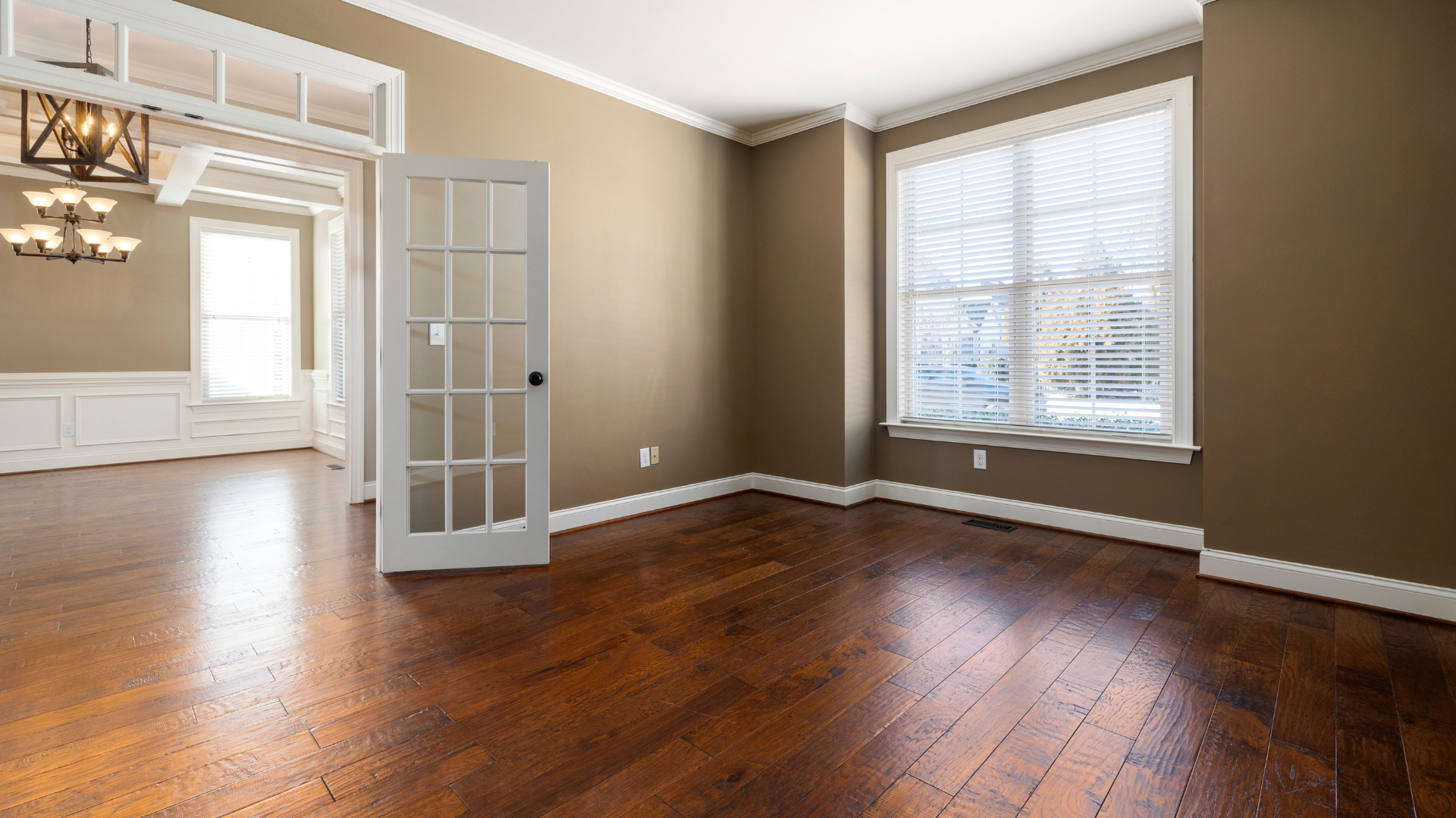 Chambre vide avec parquet, murs marron, garnitures blanches et une fenêtre.
