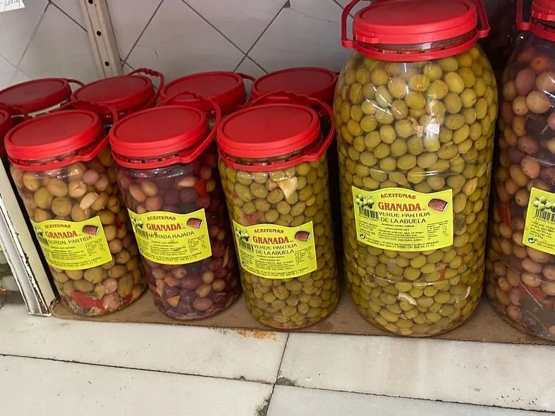 Tarros de aceitunas con tapas rojas en un estante, aceitunas verdes y oscuras.
