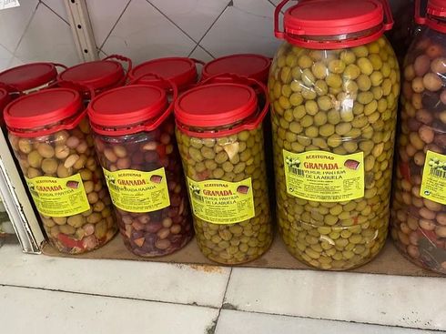 Tarros de aceitunas con tapas rojas en un estante, aceitunas verdes y oscuras.