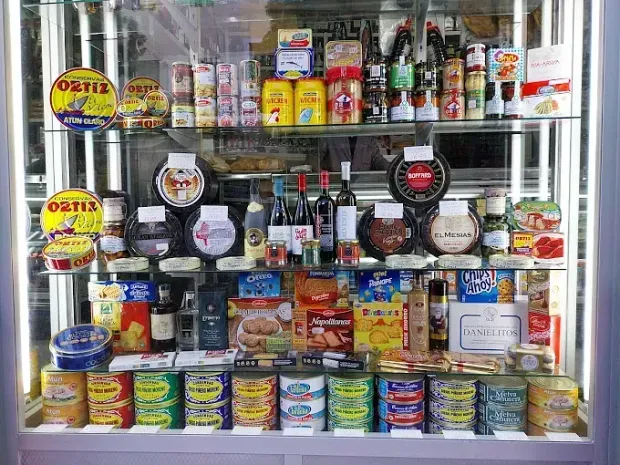 Vitrina llena de diversos productos enlatados, botellas y alimentos envasados en un entorno de tienda.