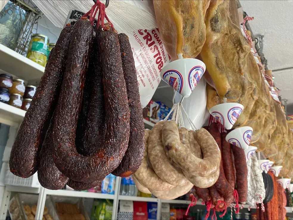 Filas de salchichas y jamón curado colgados en una tienda de delicatessen; de color rojo oscuro, marrón claro y varios colores.