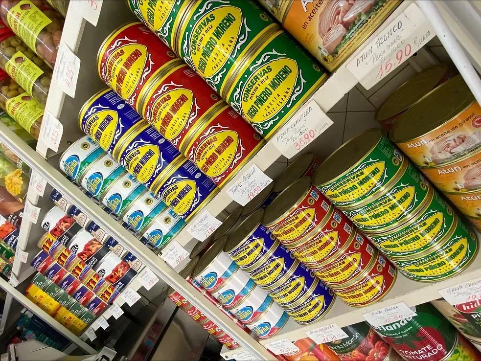 Estantes repletos de productos enlatados de colores, incluidas latas verdes, rojas y azules, en un entorno de tienda.
