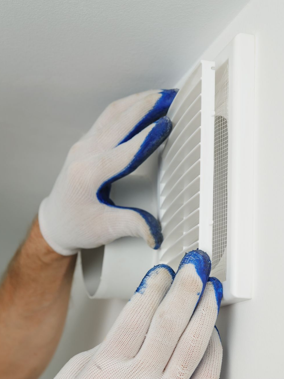 Une personne portant des gants installe une grille d'aération blanche sur un mur.