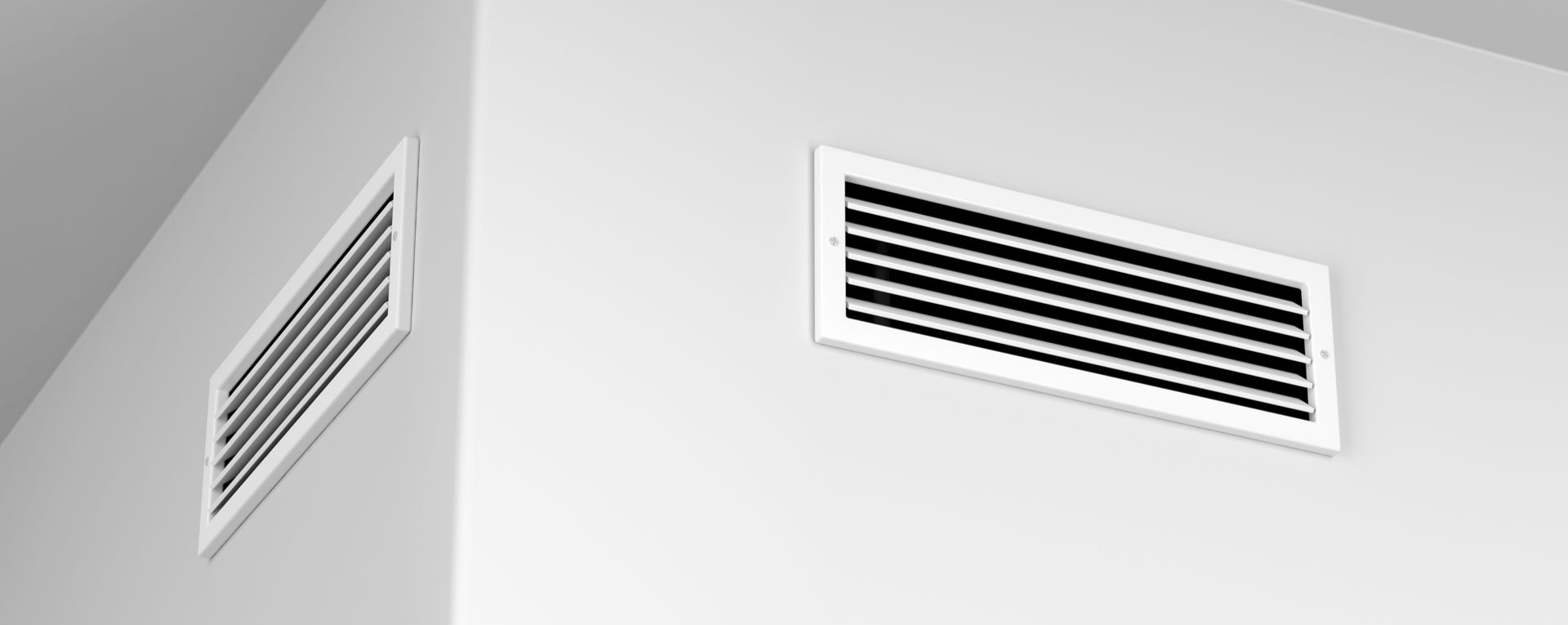 Deux grilles d'aération blanches à lamelles noires sur un mur blanc.