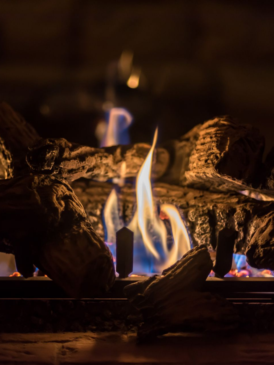 Flammes de cheminée s'élevant de bûches décoratives dans une ambiance sombre.