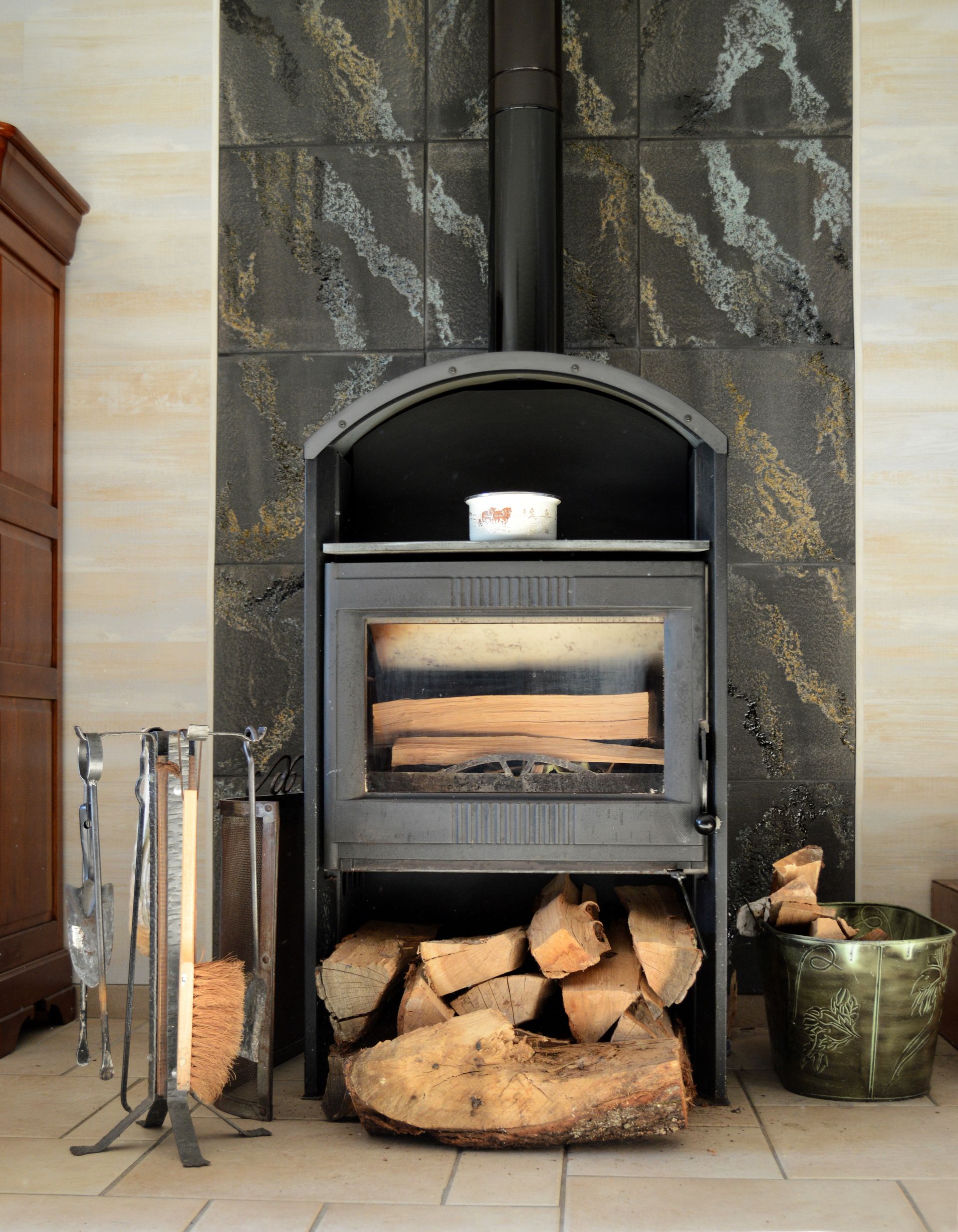 Cheminée avec bûches empilées, outils en métal et carreaux muraux décoratifs.