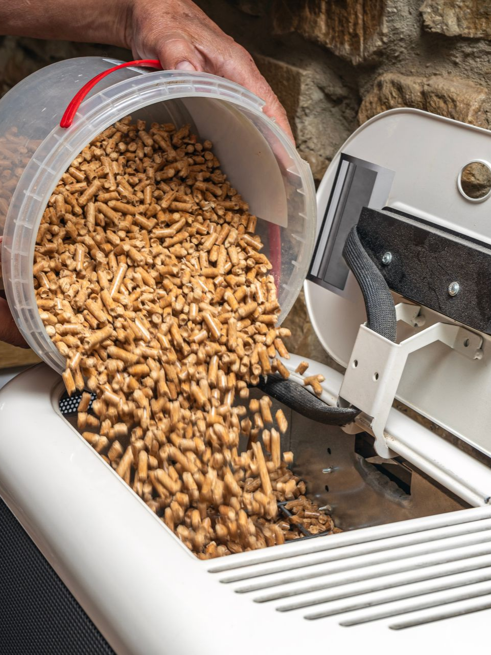 Une personne verse des granulés de bois d'un seau dans un poêle à granulés.