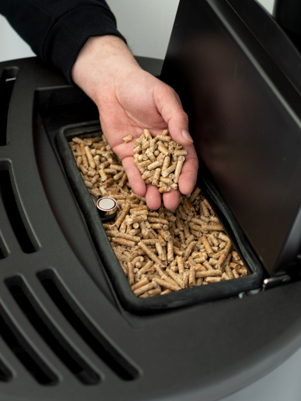 Remplissage manuel d'un poêle à granulés de bois avec des granulés bruns.