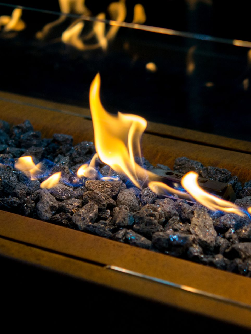 Des flammes dansent au-dessus de verre à feu bleu foncé dans un long foyer métallique.