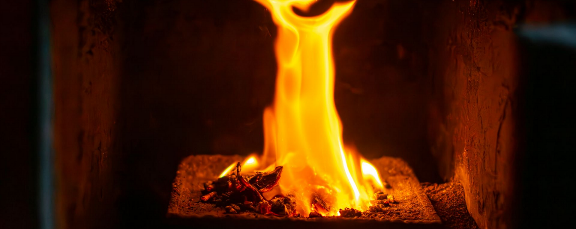 Des flammes brûlent dans une cheminée sombre.