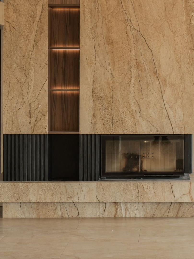 Cheminée avec façade en marbre, étagères intégrées, meuble sombre et feu allumé.