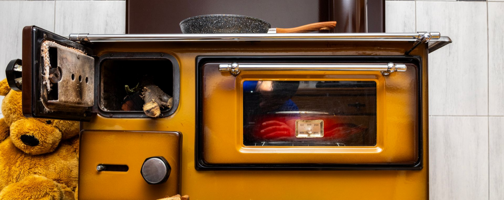 Poêle jaune avec four et foyer ouvert. Un ours en peluche est assis à côté du poêle.