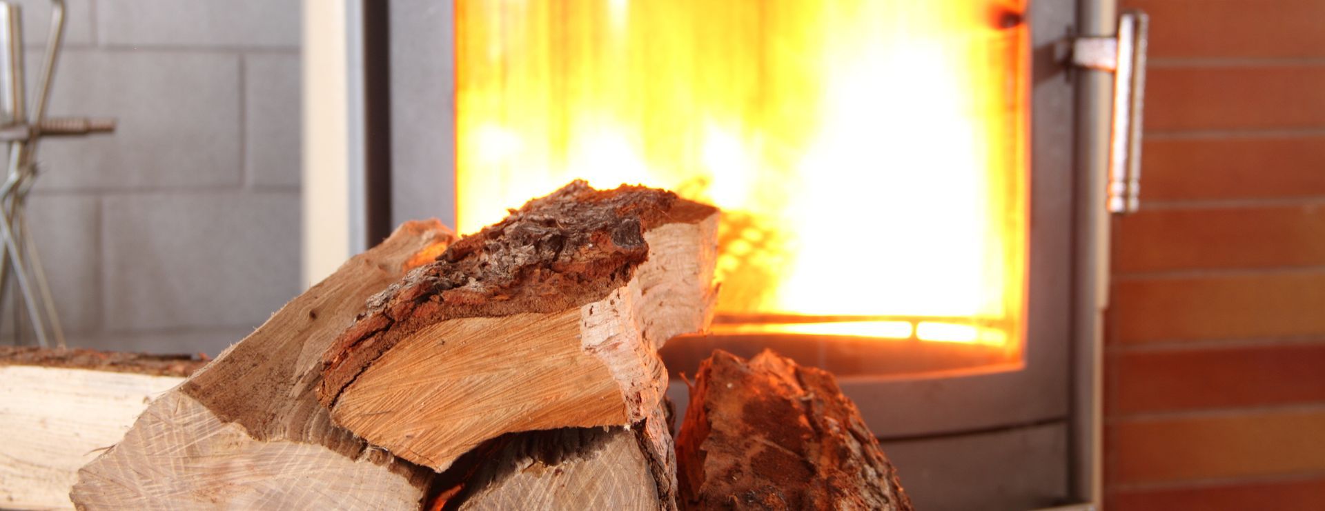 Cheminée avec des flammes ardentes et une pile de bois au premier plan.