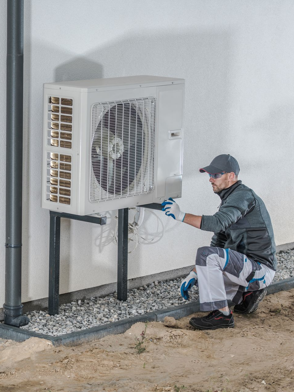 Un homme installe une pompe à chaleur extérieure sur un bâtiment.