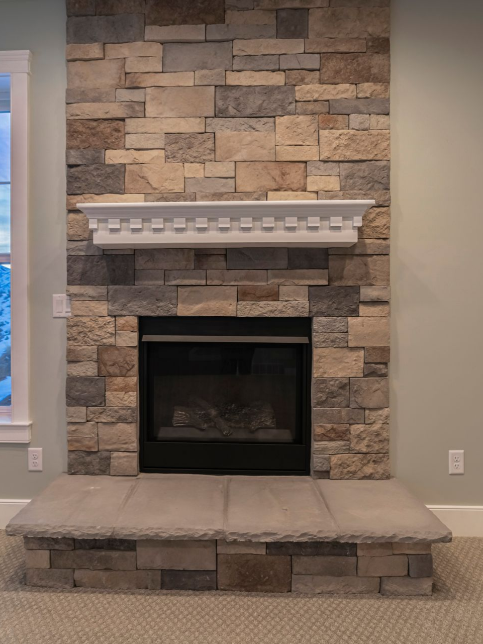 Cheminée en pierre avec intérieur noir, manteau blanc et foyer gris.