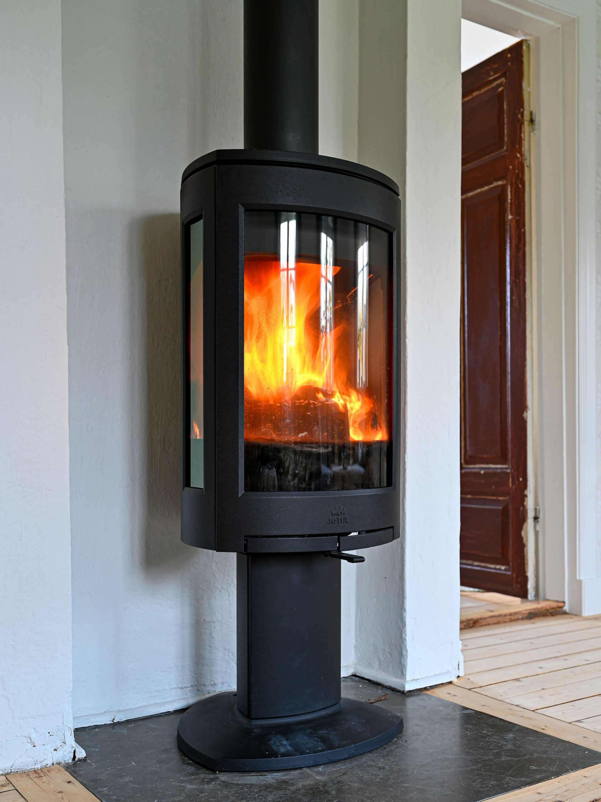 Un poêle à bois noir avec un feu incandescent dans une pièce près d'une porte.