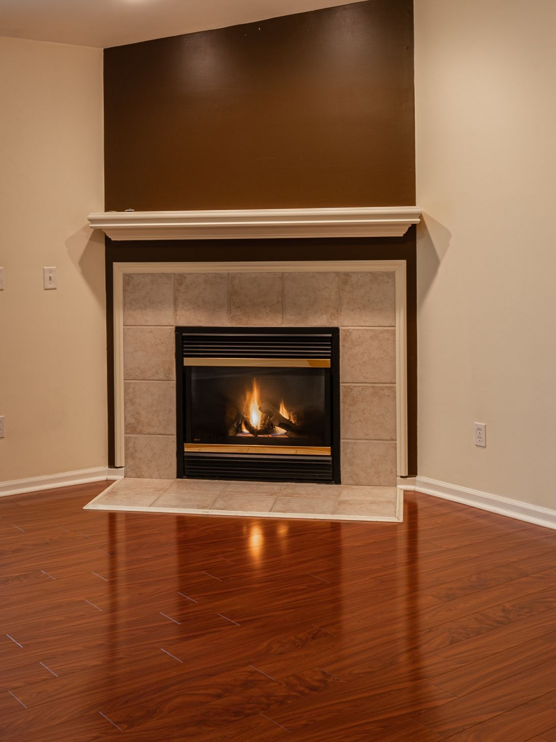 Cheminée avec flammes ardentes, mur d'accent marron, carrelage beige, manteau blanc et parquet brillant.