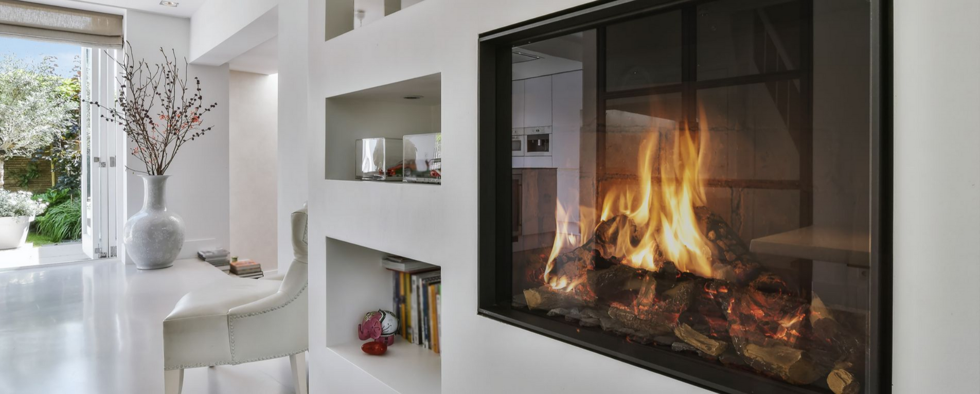 Espace de vie moderne et blanc avec cheminée, étagères et vue sur un jardin.