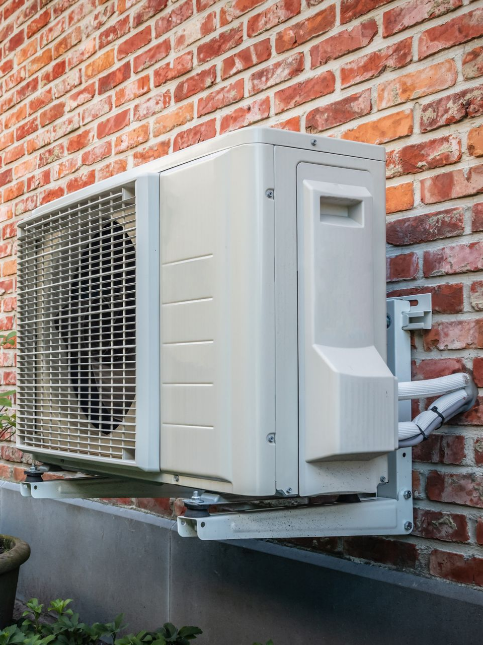 Unité de climatisation extérieure montée sur un mur de briques.
