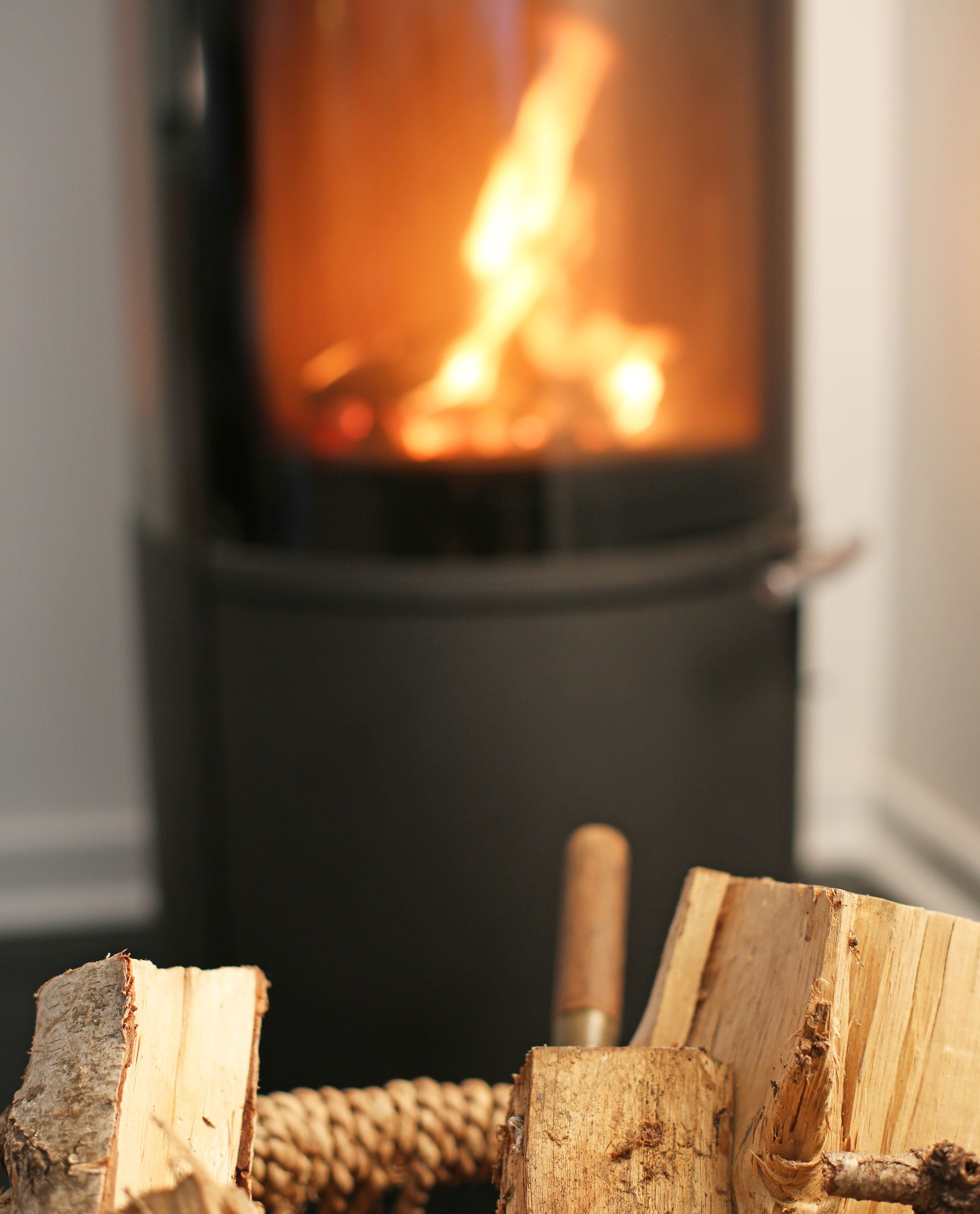Feu brûlant dans un poêle noir ; bûches fendues dans un panier au premier plan.