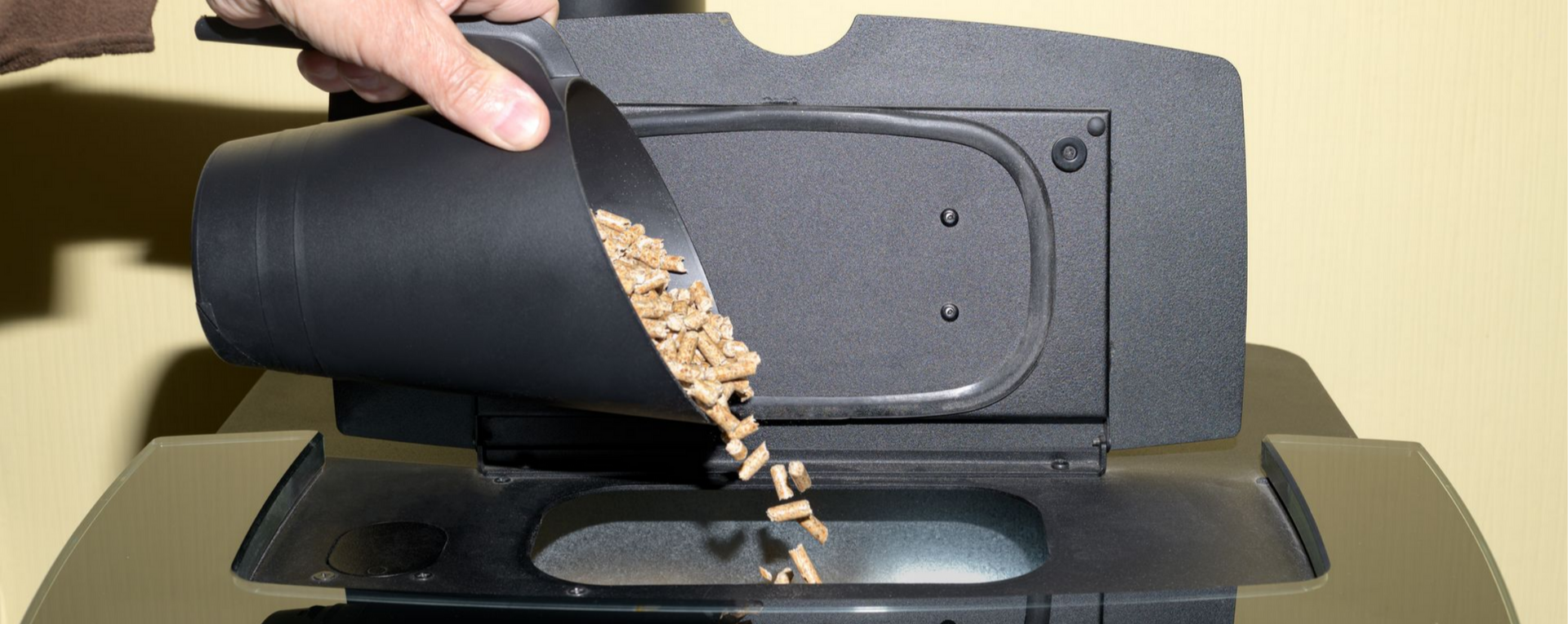 Une personne verse des granulés de bois à l'aide d'une pelle dans un poêle à granulés.