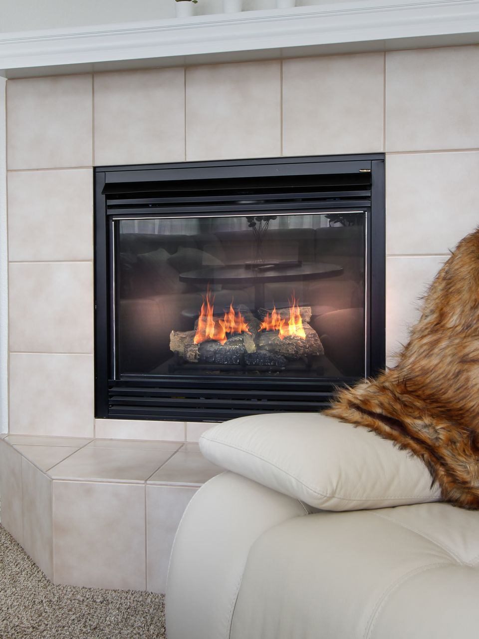 Cheminée avec bûches incandescentes, cadre noir, entourage en carrelage beige.