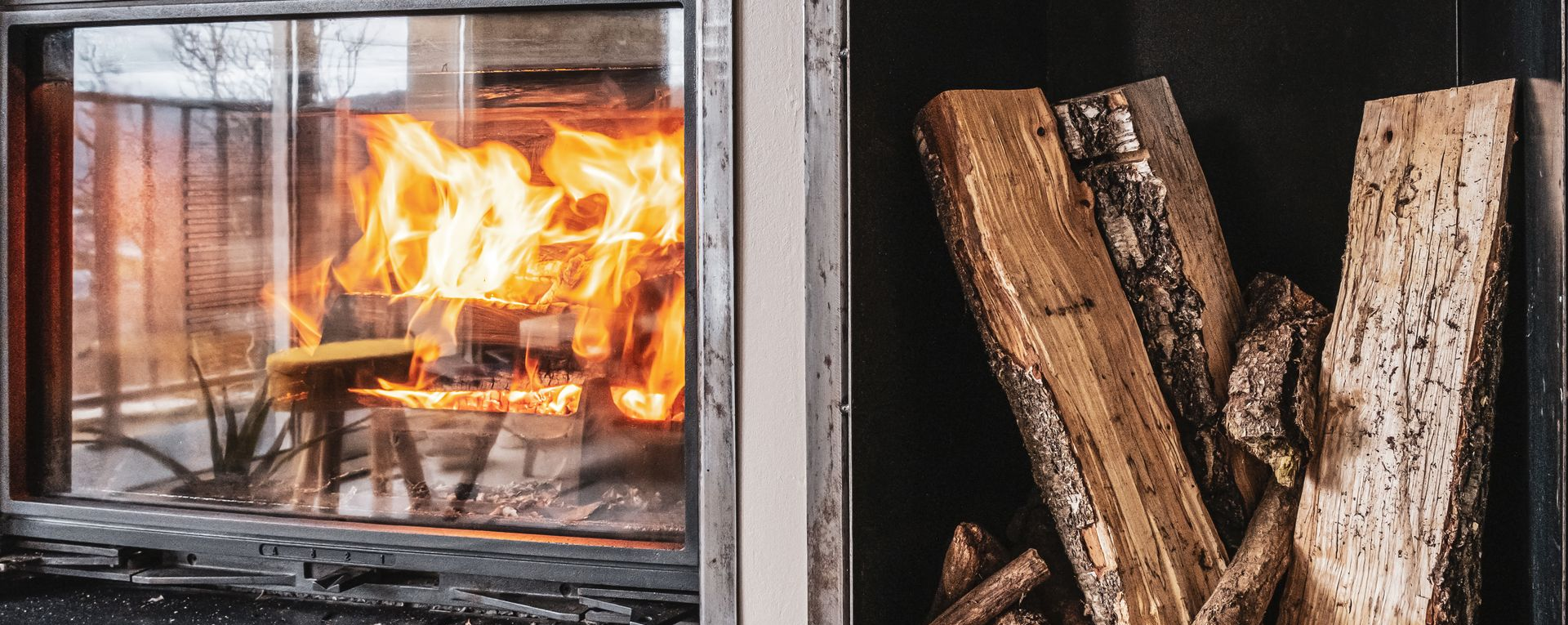 Une cheminée avec des flammes à gauche et du bois de chauffage empilé à droite, séparées par une paroi verticale.