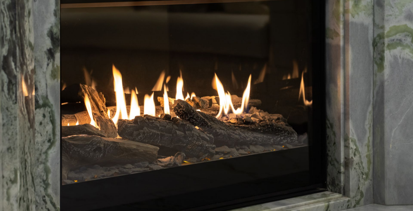 Cheminée aux flammes vacillantes derrière une vitre, encadrée de marbre vert.