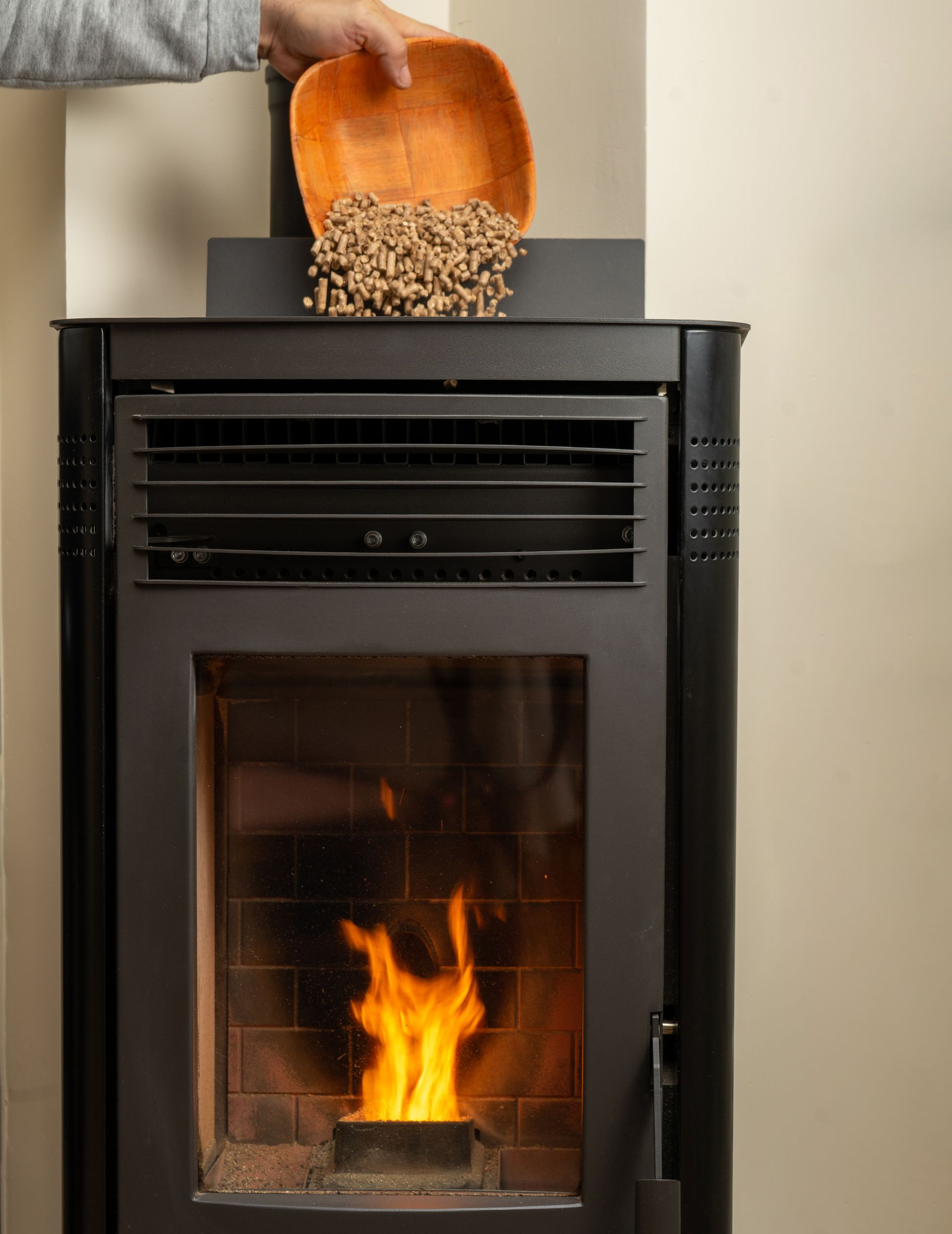 Une personne verse des granulés de bois dans un poêle à granulés allumé.