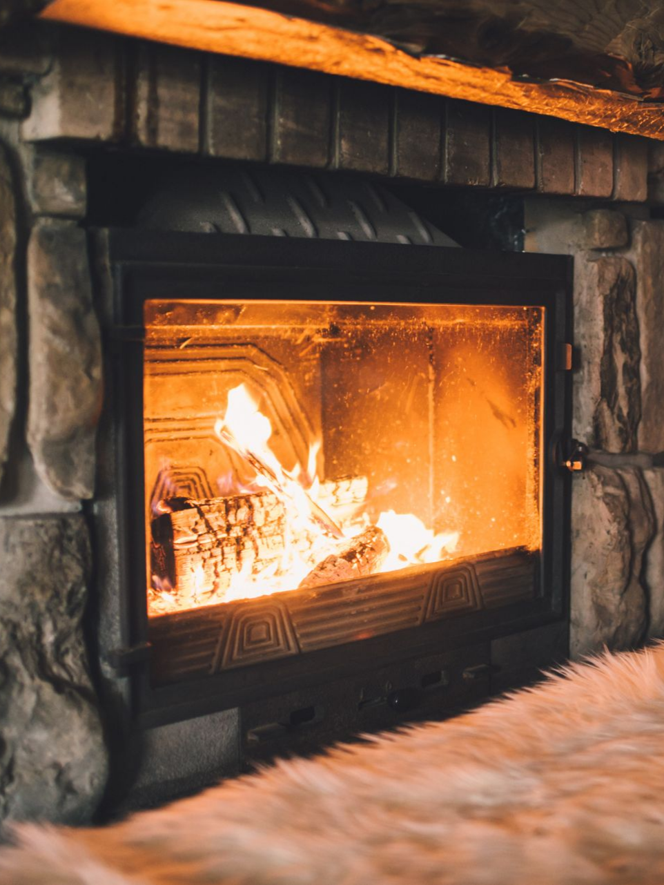 Cheminée avec du bois qui brûle, entourage en pierre, diffusant une chaude lueur orangée.