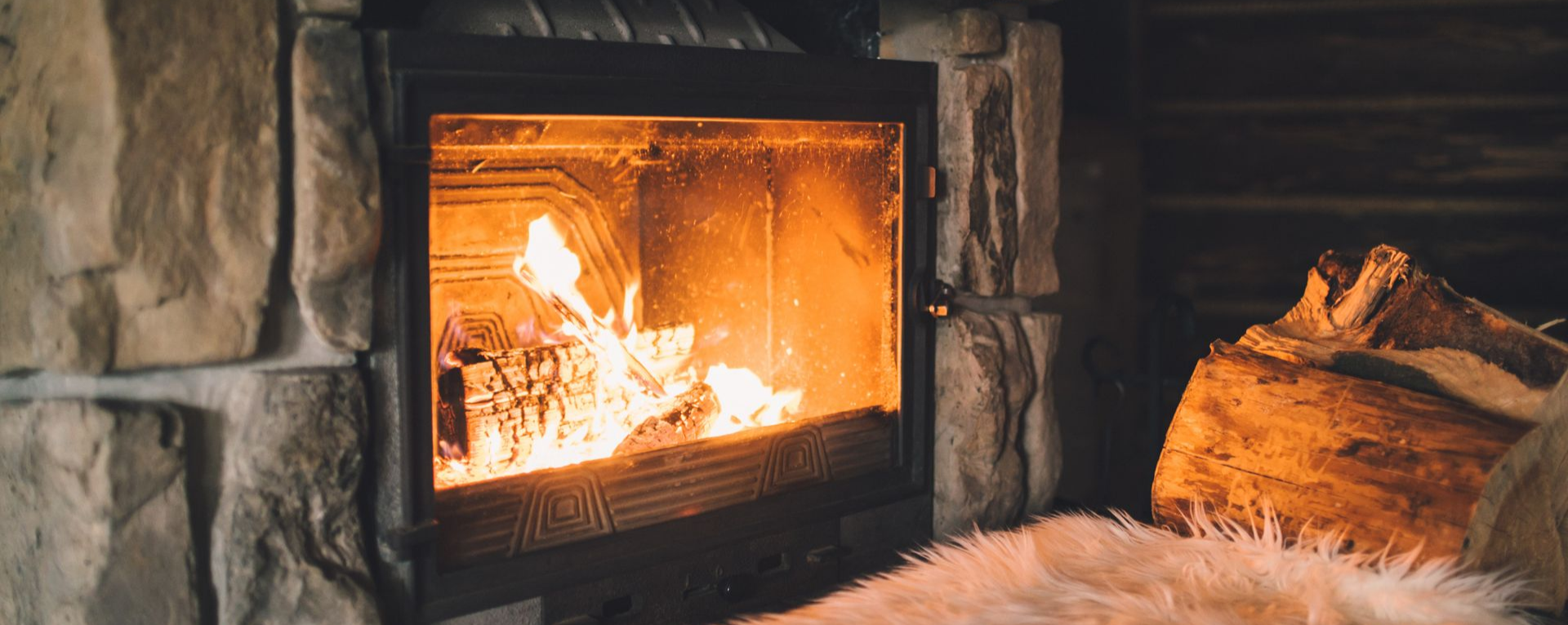 Cheminée avec bûches incandescentes, entourage en pierre.