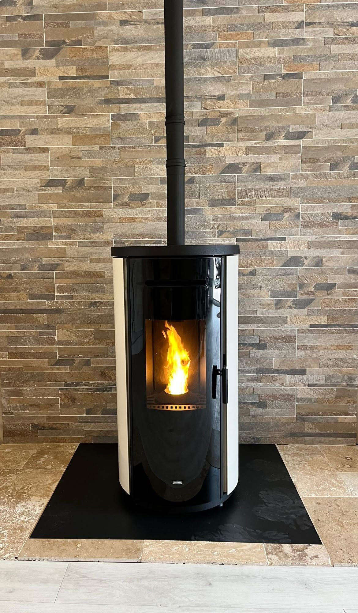 Poêle à granulés noir avec vitre, à côté d'un seau de granulés, sur une surface carrelée.