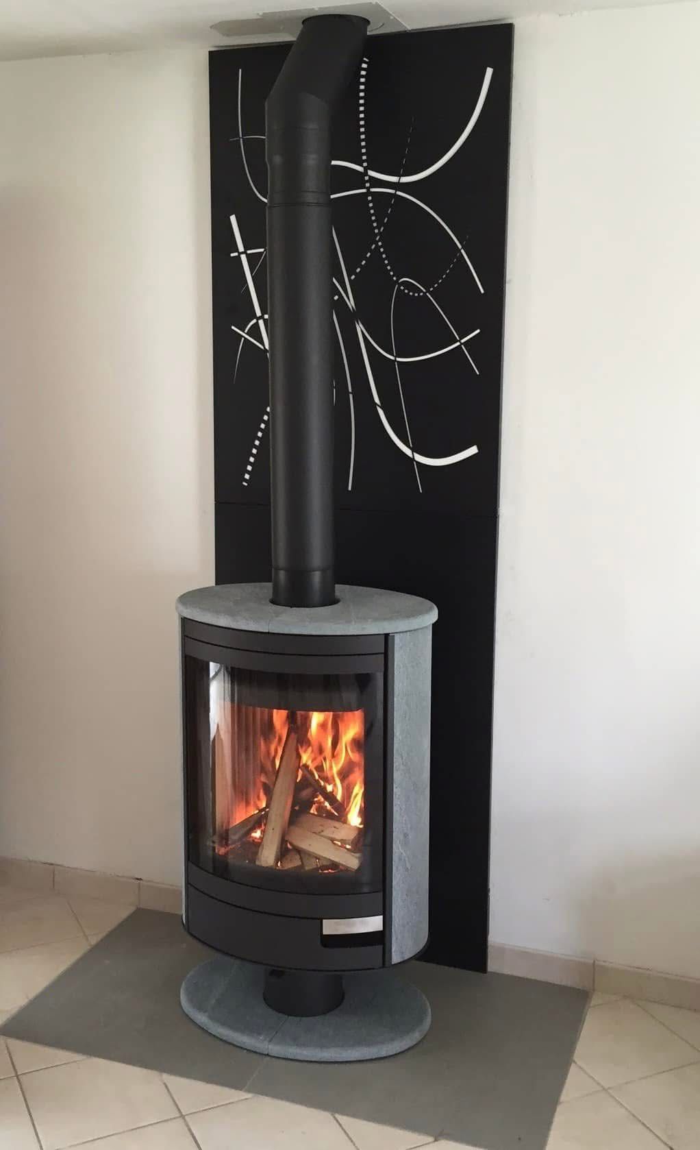 Poêle à bois noir aux flammes visibles, rangement pour le bois en dessous, sur un tapis devant un mur blanc.