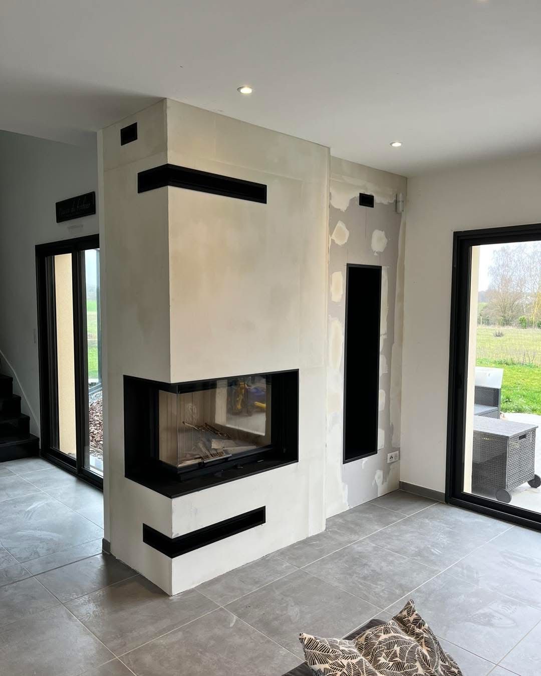 Pièce confortable avec une cheminée allumée, un fauteuil avec une couverture et un oreiller, et du bois de chauffage empilé.