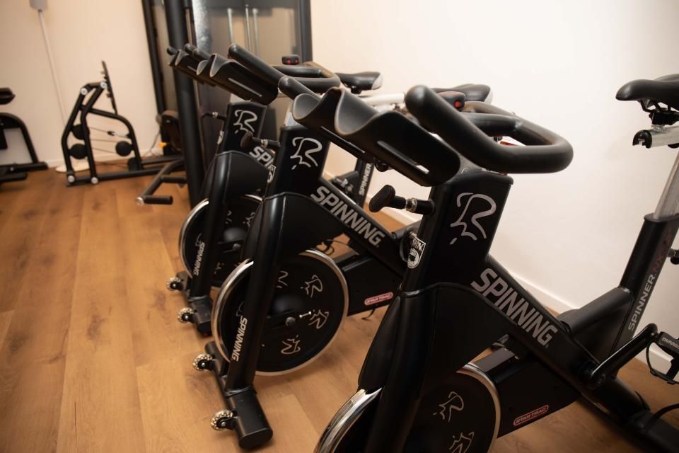 Indoor-Cycling-Bikes in einem Fitnessstudio, schräge Ansicht mit Holzboden und weissen Wänden.
