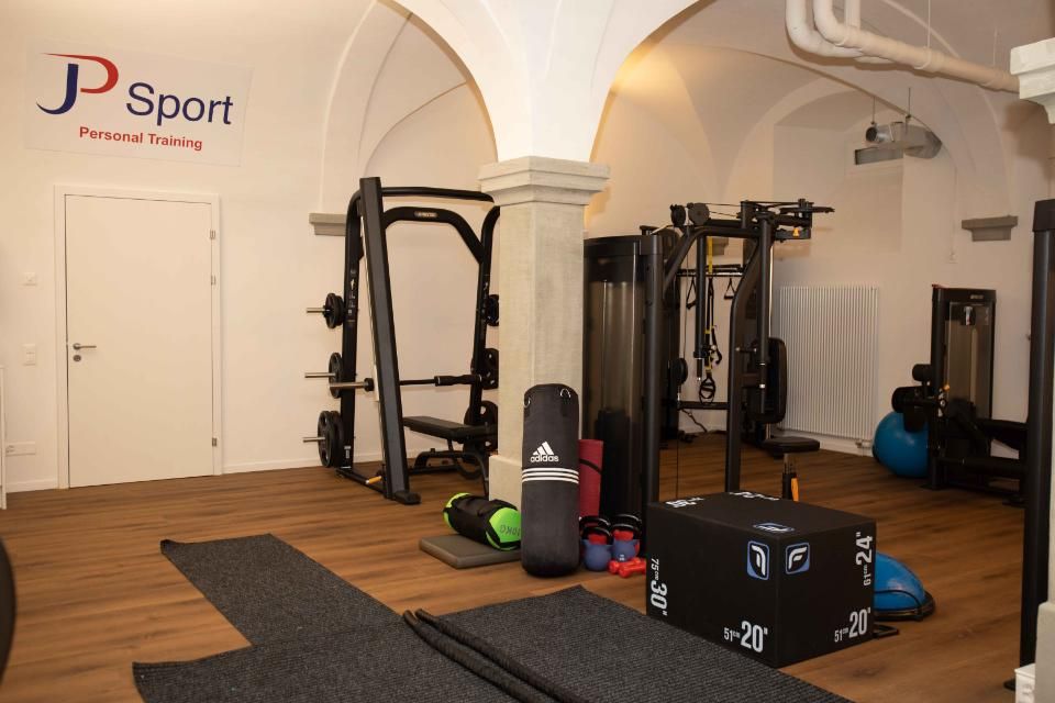 Innenraum einer Turnhalle mit Krafttrainingsgeräten, Matten und Boxsack unter einer gewölbten Decke.